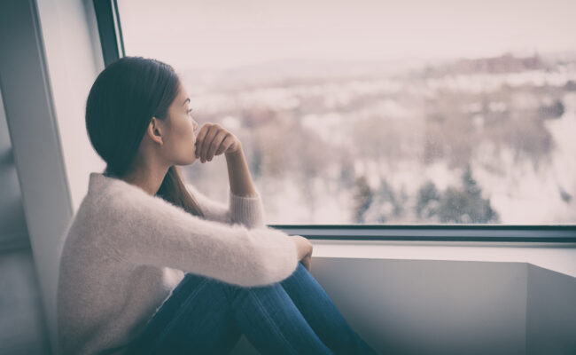 Kobieta z osobowością introwertyczną siedzi sama na parapecie i patrzy przez okno