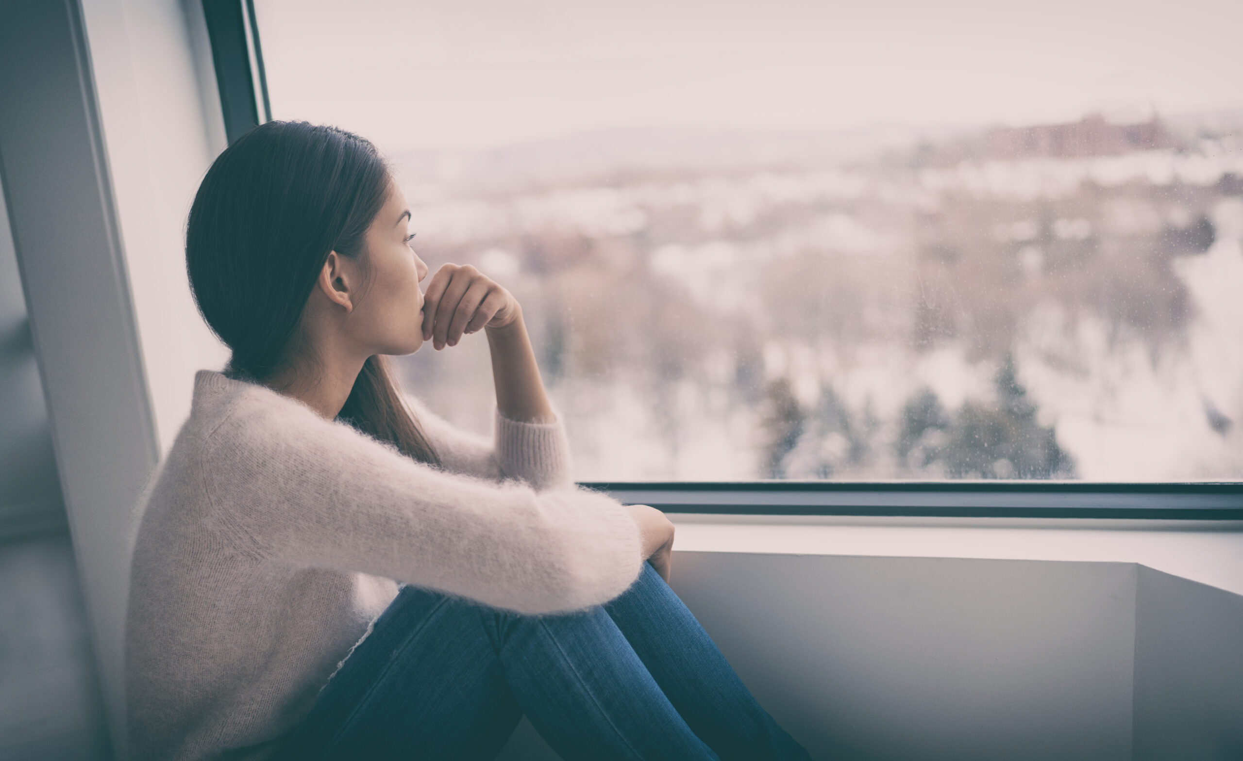 Kobieta z osobowością introwertyczną siedzi sama na parapecie i patrzy przez okno